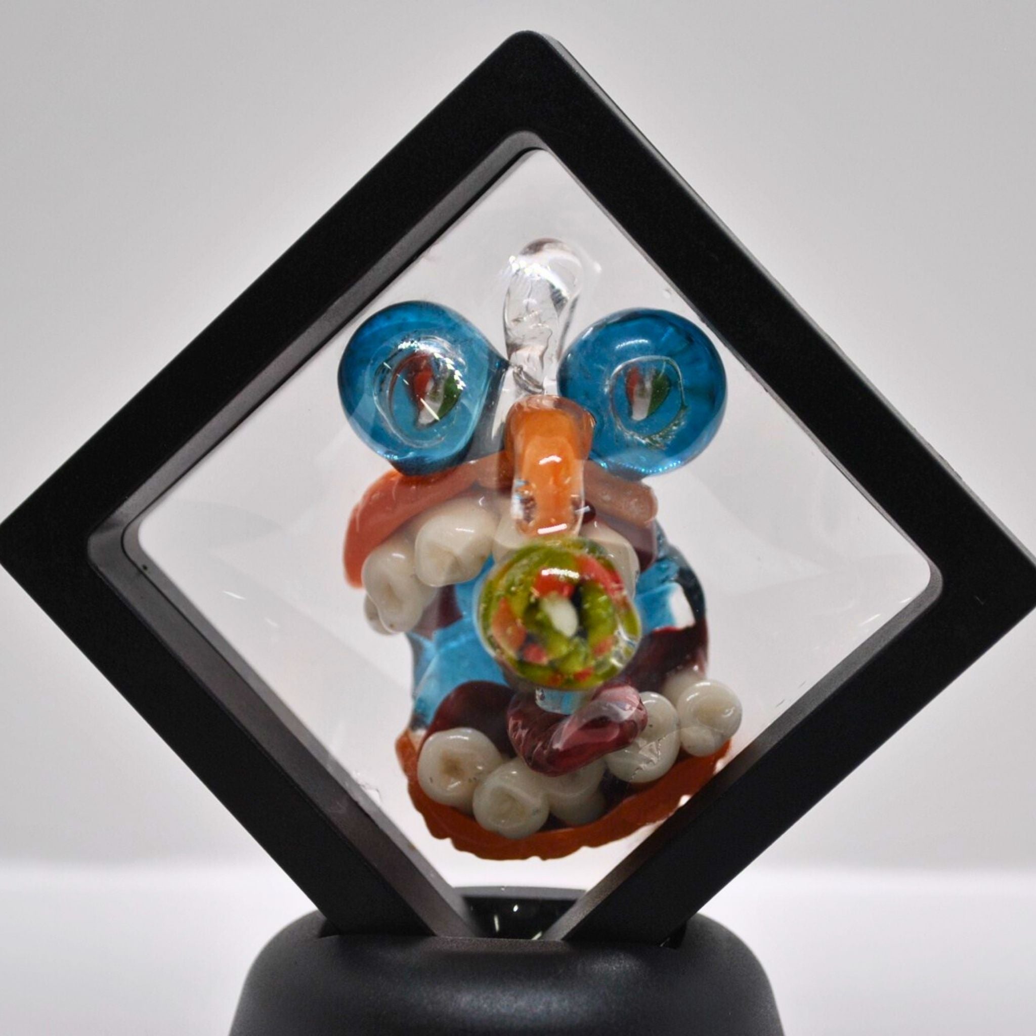 Colorful glass pendant with intricate designs on a black stand against a white background