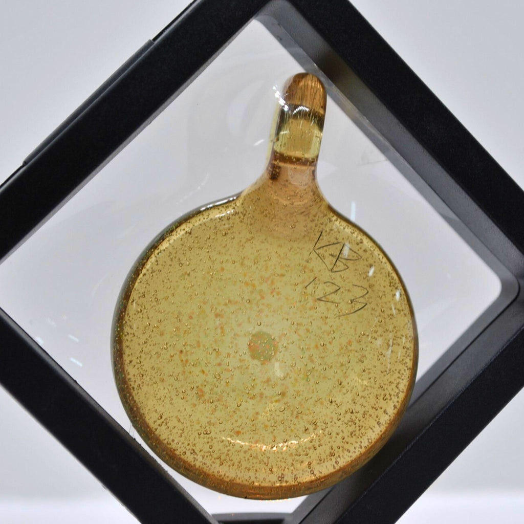 Gold-colored pendant with speckled texture in a display case