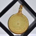 Gold-colored pendant with speckled texture in a display case