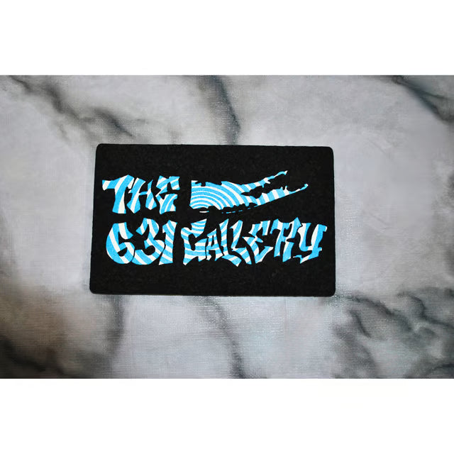 A black rectangular mat or plaque featuring the text 'THE 631 GALLERY' in a stylized light blue and white patterned font, placed on a gray marble surface.