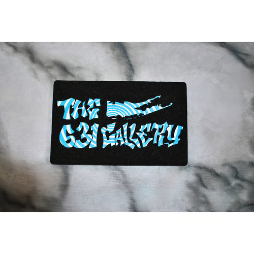 A black rectangular mat or plaque featuring the text 'THE 631 GALLERY' in a stylized light blue and white patterned font, placed on a gray marble surface.