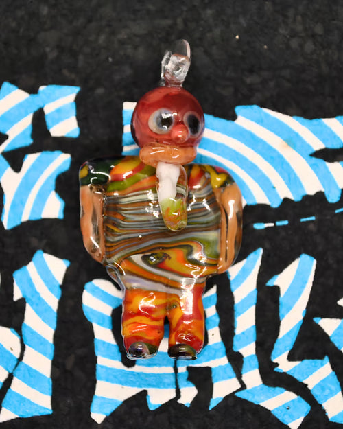 A hand-blown glass figurine of a stylized person with a red head, striped torso in orange, yellow, green, and brown, and patterned legs, set against a black background with blue and white graphic shapes.