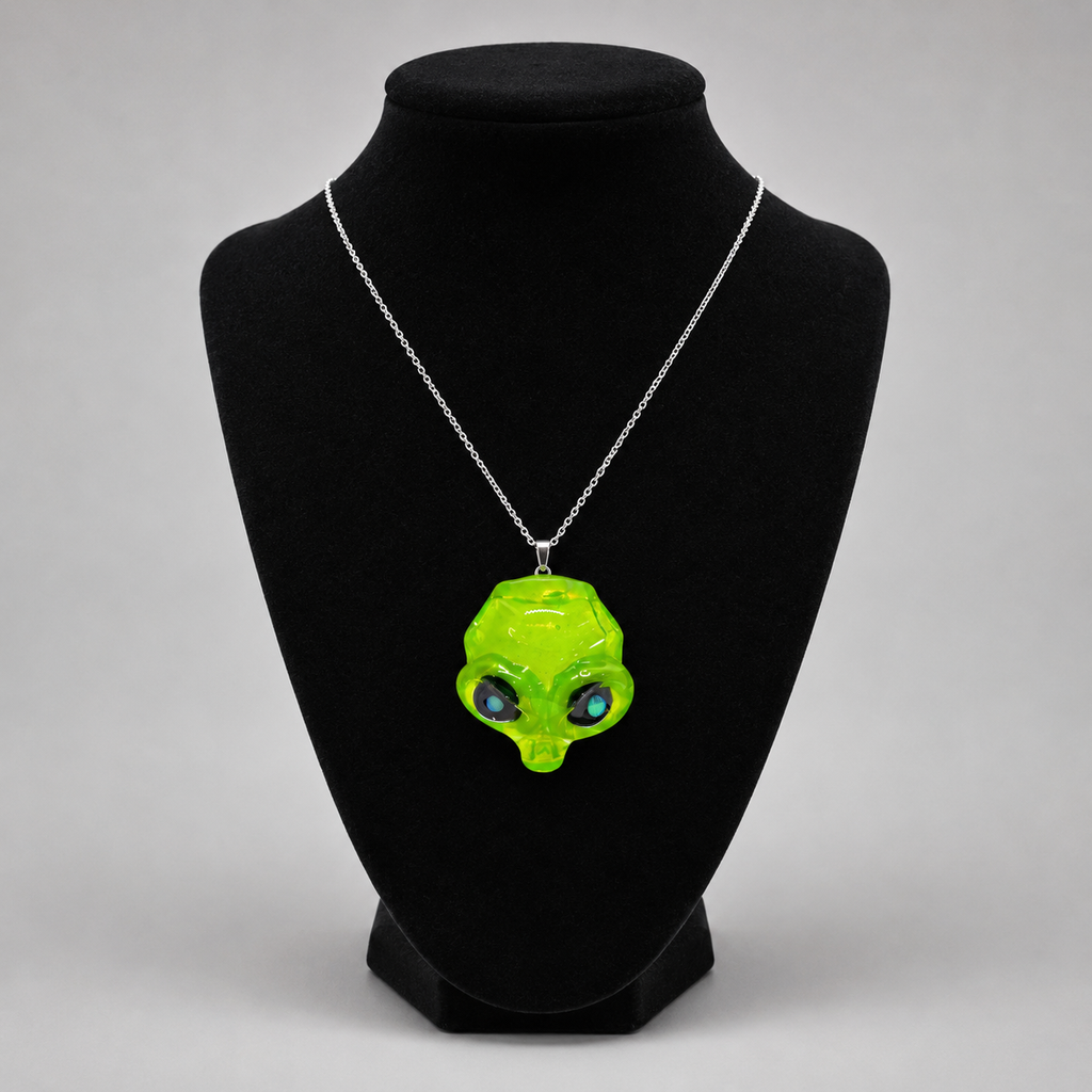 A neon green alien head pendant necklace on a silver chain, displayed on a black velvet jewelry bust against a light gray background.
