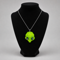 A neon green alien head pendant necklace on a silver chain, displayed on a black velvet jewelry bust against a light gray background.