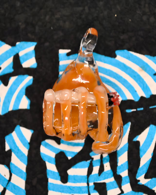 A  glass hand with orange-colored translucent wraps and a small red accent, shown against a black background with a blue-and-white graphic print.