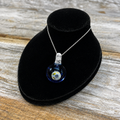 A silver chain necklace with a clear glass bubble pendant containing a miniature blue and white globe, displayed on a black velvet jewelry bust over a rustic wooden surface.