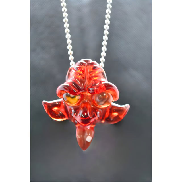 A red translucent glass monster pendant necklace with a silver ball chain, shown against a dark gray background.