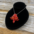 A red translucent dragon pendant necklace on a silver ball chain, displayed on a black velvet jewelry bust over a rustic wooden surface.