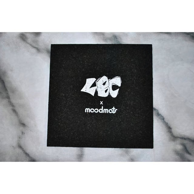 A square black textured box featuring the stylized white 'LBC' logo and 'moodmat' text, placed on a light gray marble-patterned surface.