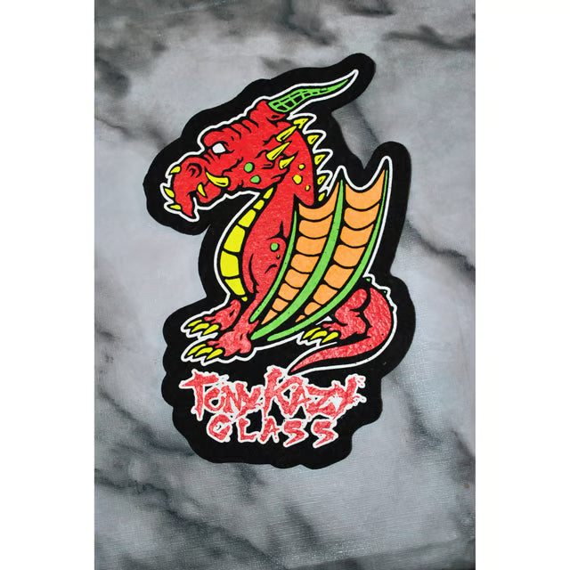 A die-cut embroidered patch featuring a red dragon with green and yellow accents and the text 'Tony Kazy Glass' in red, shown on a gray marble-patterned background.