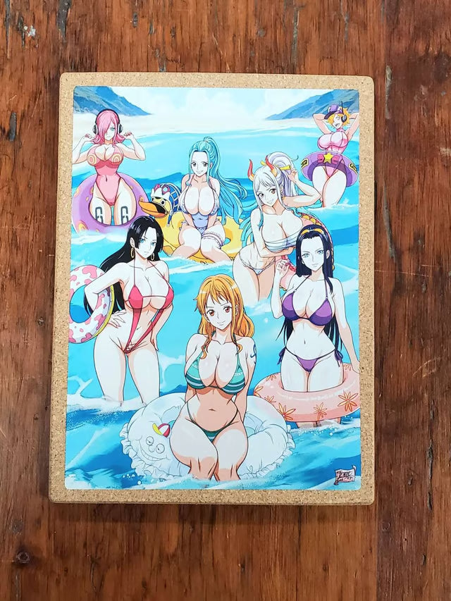 A rectangular printed art piece or book cover featuring colorful anime-style illustrated women in swimwear on a beach, photographed from above on a dark wooden surface.
