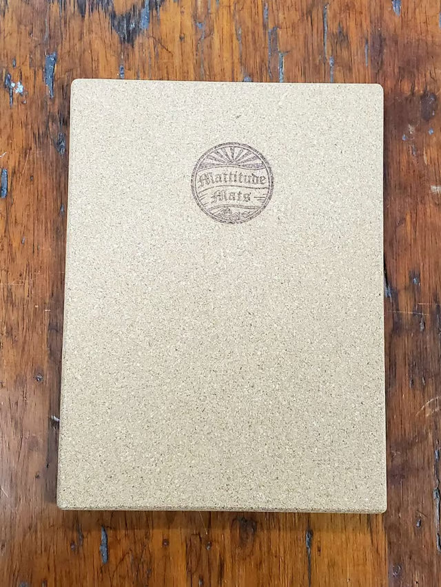 A hardcover notebook with a textured beige cover and a circular embossed logo reading 'Latitude 37.23' on a rustic wooden table.