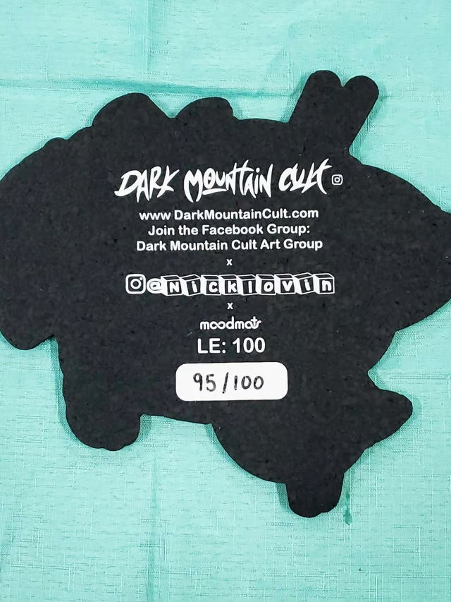 A black die-cut sticker or decal featuring the text 'Dark Mountain Cult' and website/social details, placed on a light aqua textured background.