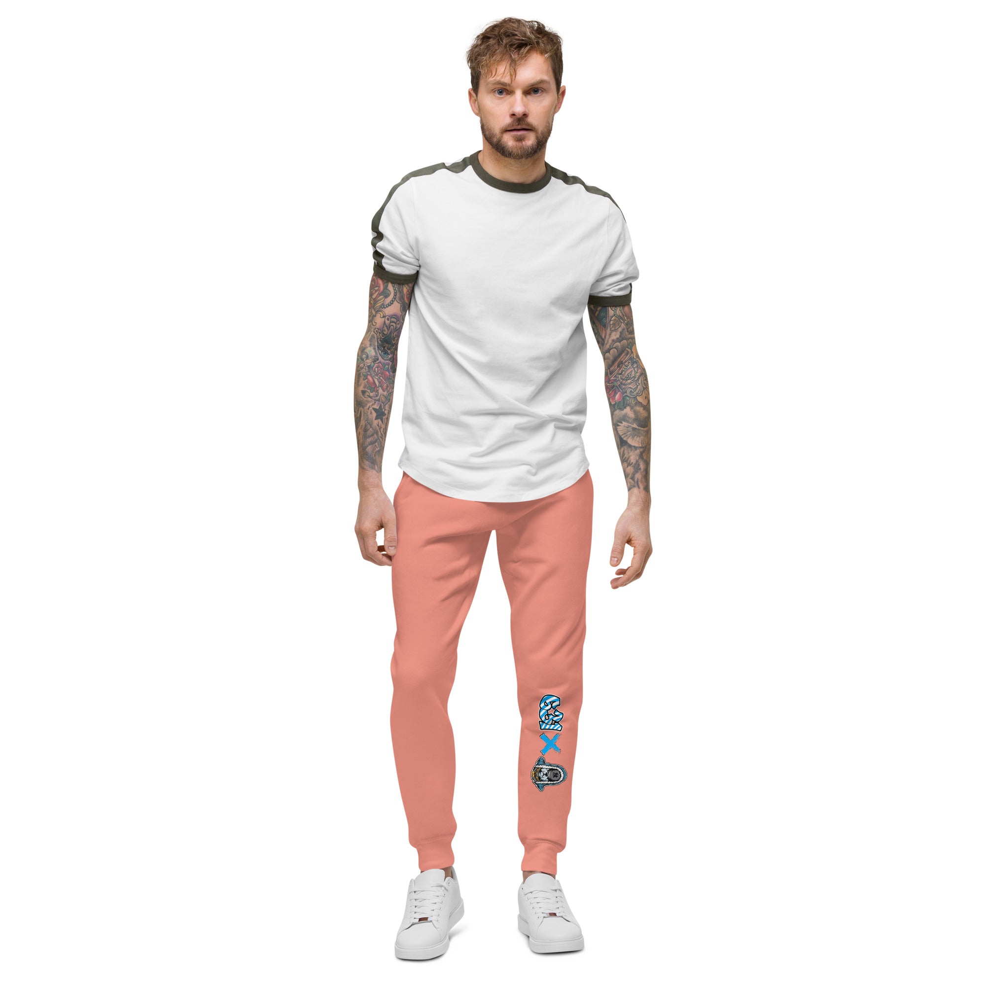 Man wearing a white t-shirt and pink pants with tattoos on arms and legs, standing against a white background